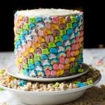 A lucky charms cake sitting on a pedestal inside a bowl of lucky charms.