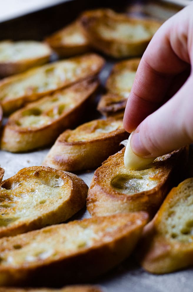 A hand rubbing garlic onto a piece of homemade garlic toast