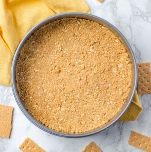 Overhead of a springform pan with a graham cracker crust. Broken graham crackers surround it.