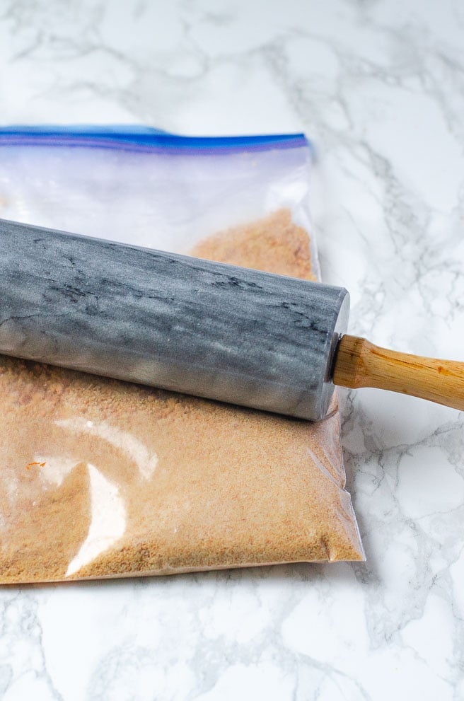 a gray rolling pin making graham cracker crumbs in a plastic bag