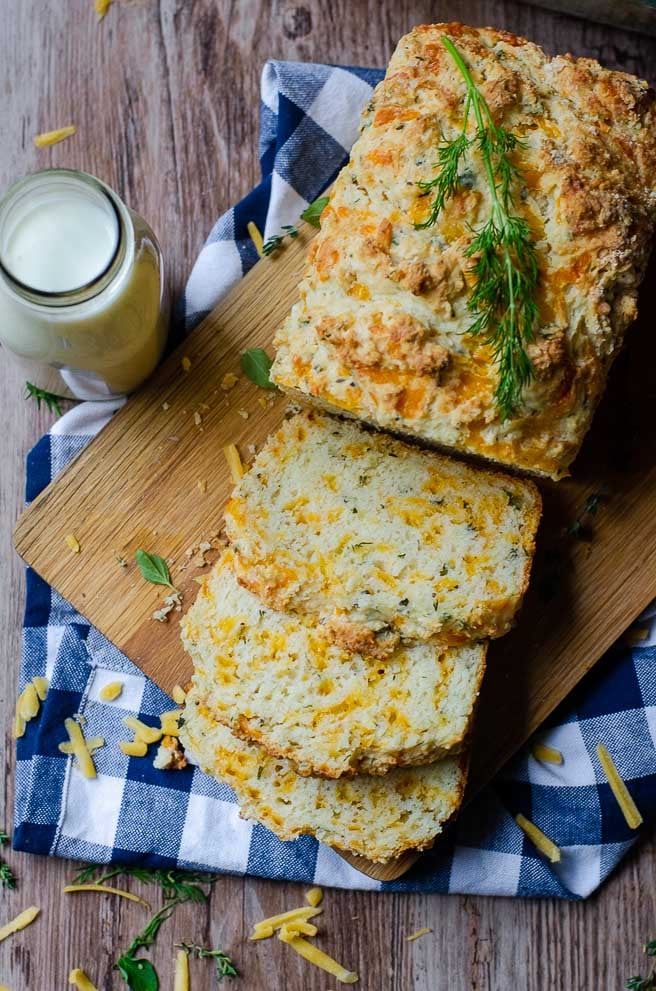 overhead view of a sliced loaf of buttermilk quick bread on a cutting board. The board is on a blue napkin next to milk