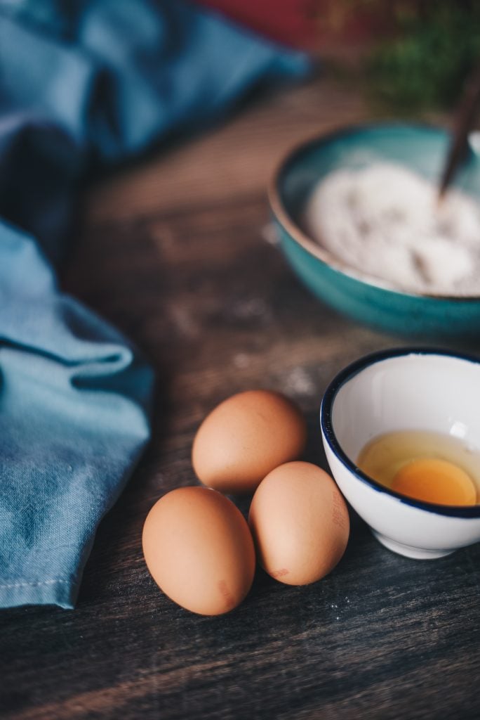 three eggs on a counter next to a bowl with a cracked egg in it.