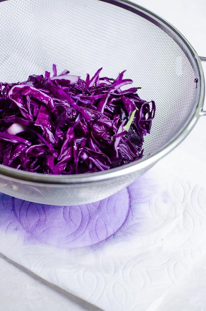 Red cabbage in a colander showing water that releases from salting.