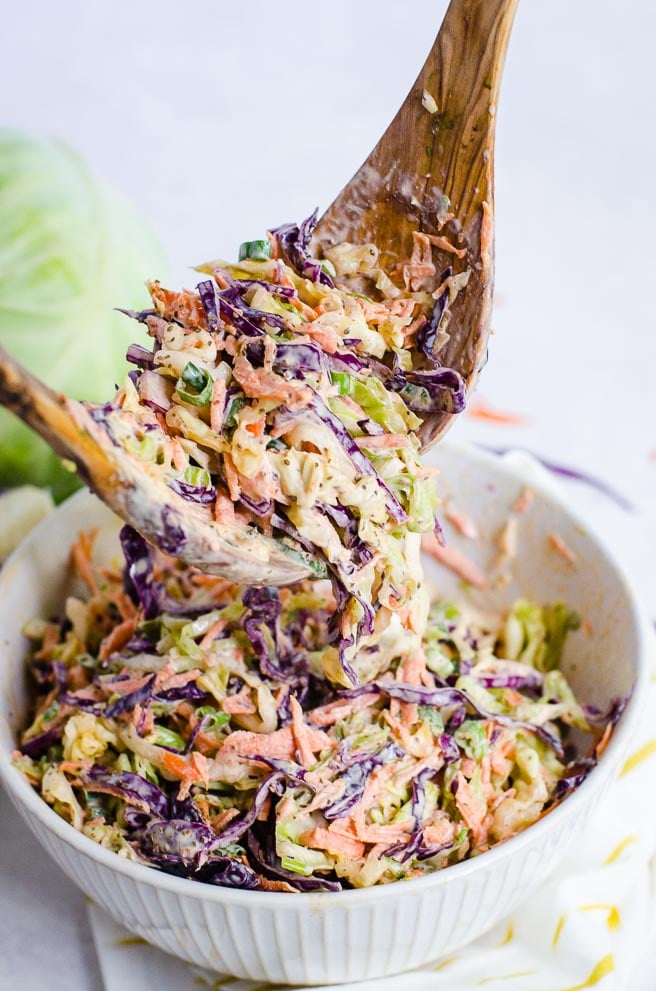 Wooden salad tongs lifting up creamy coleslaw.