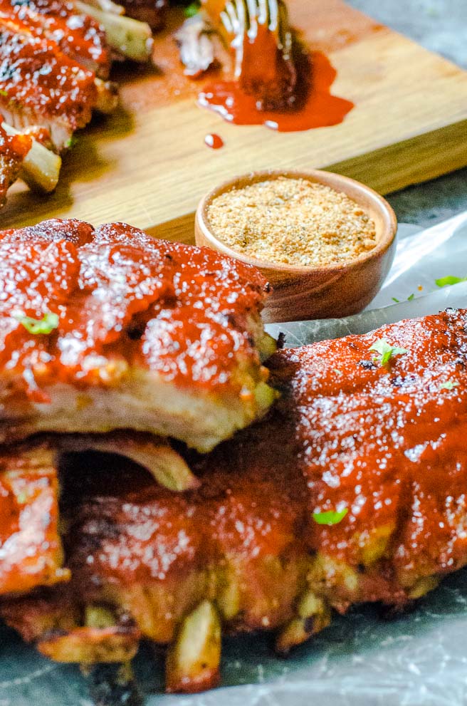 a bowl of dry rub next to cooked baby back ribs