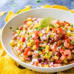 Grilled pineapple salsa in a white bowl surrounded by tortilla chips.