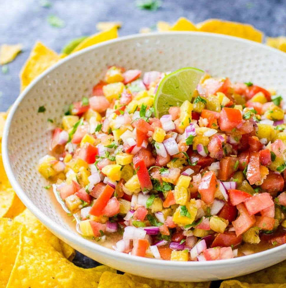 Grilled pineapple salsa in a white bowl surrounded by tortilla chips.
