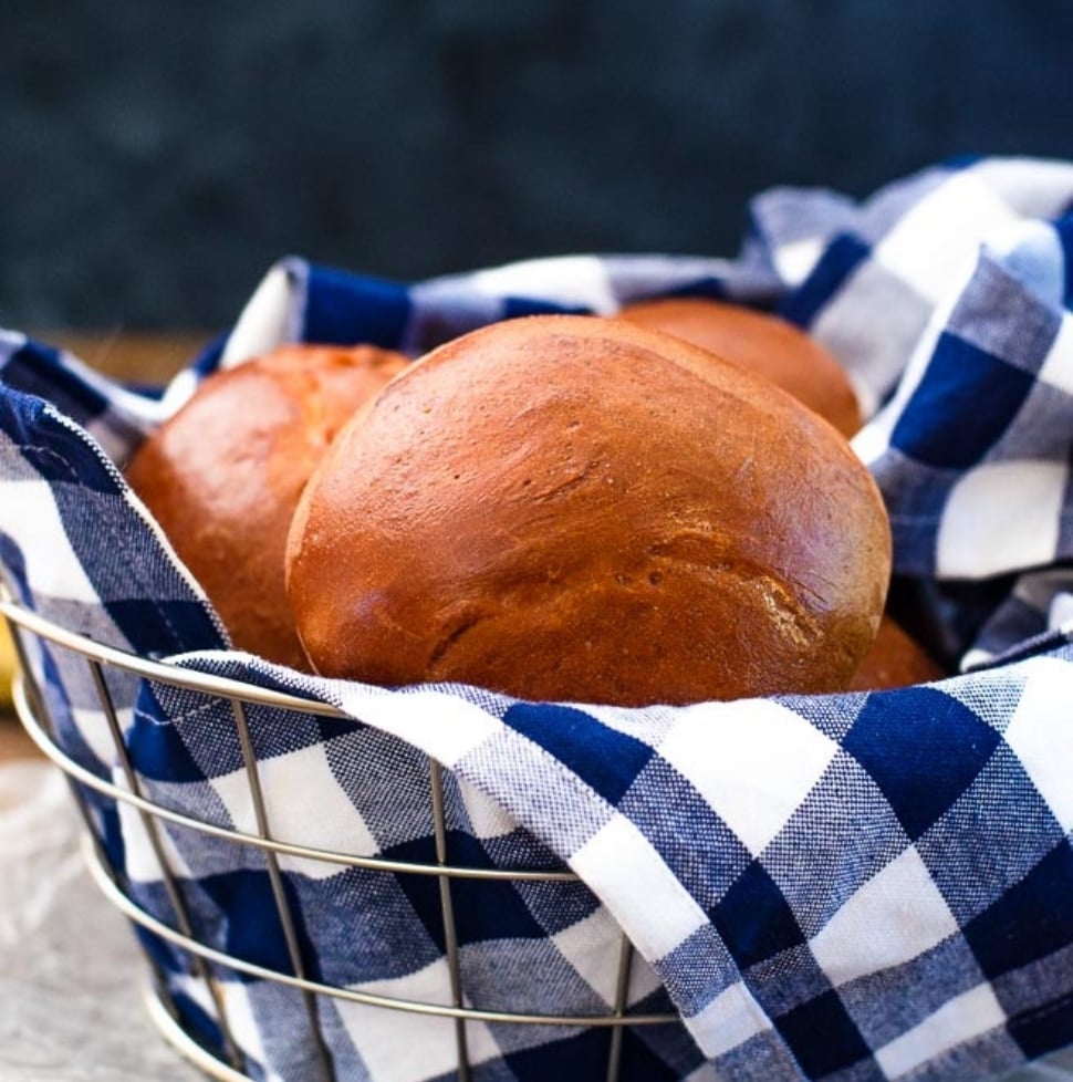 Basket of hamburger buns on a blue gingham kitchen towel.