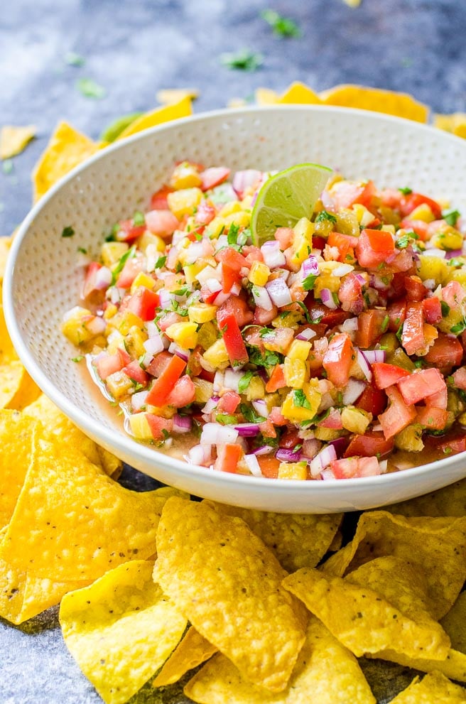 a white bowl of grilled pineapple salsa surrounded by chips