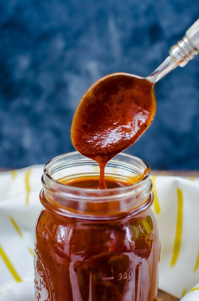 A spoon lifting homemade bbq sauce out of a mason jar