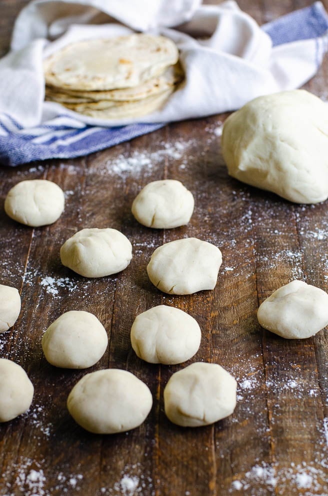 Corn tortilla dough broken into balls in front a pile of homemade corn tortillas