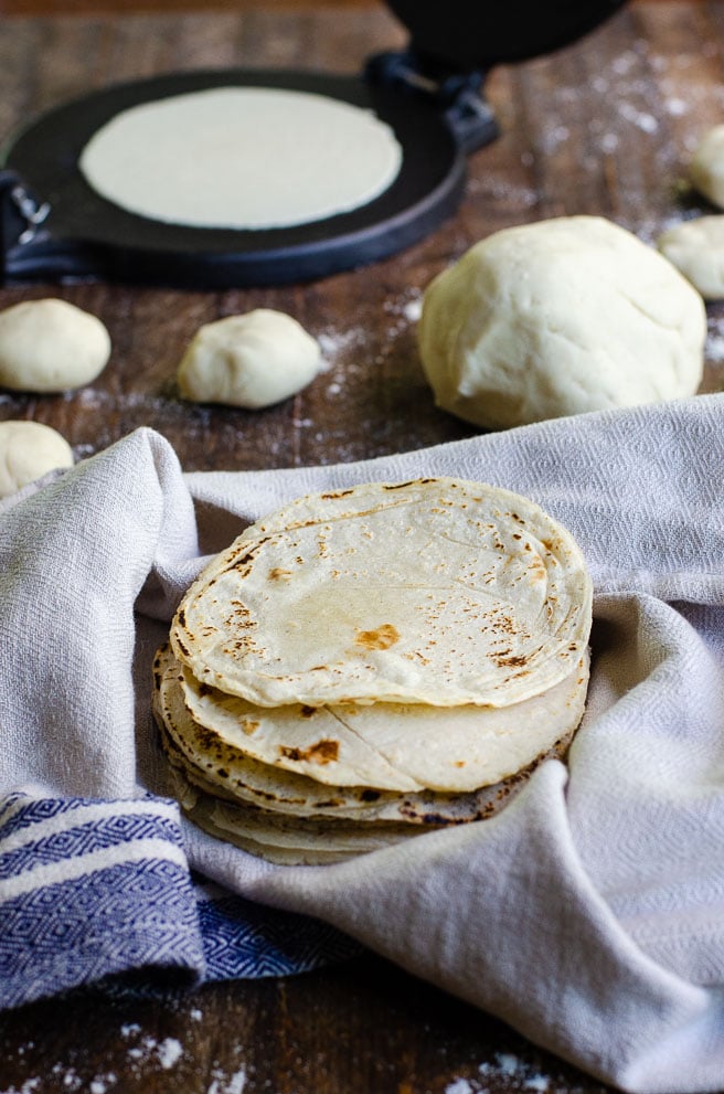 homemade corn tortillas being kept warm in front of dough and a cast iron tortilla press