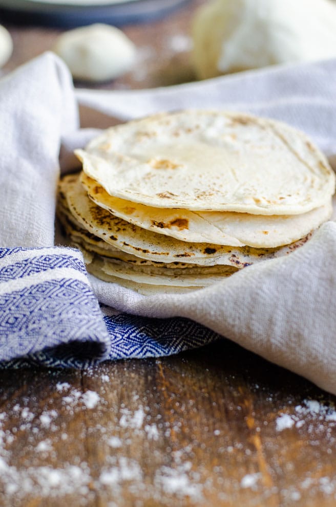 a stack of homemade corn tortillas in a tan and blue kitchen towel