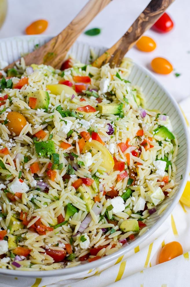 Bowl of orzo pasta salad with wooden serving spoons in it