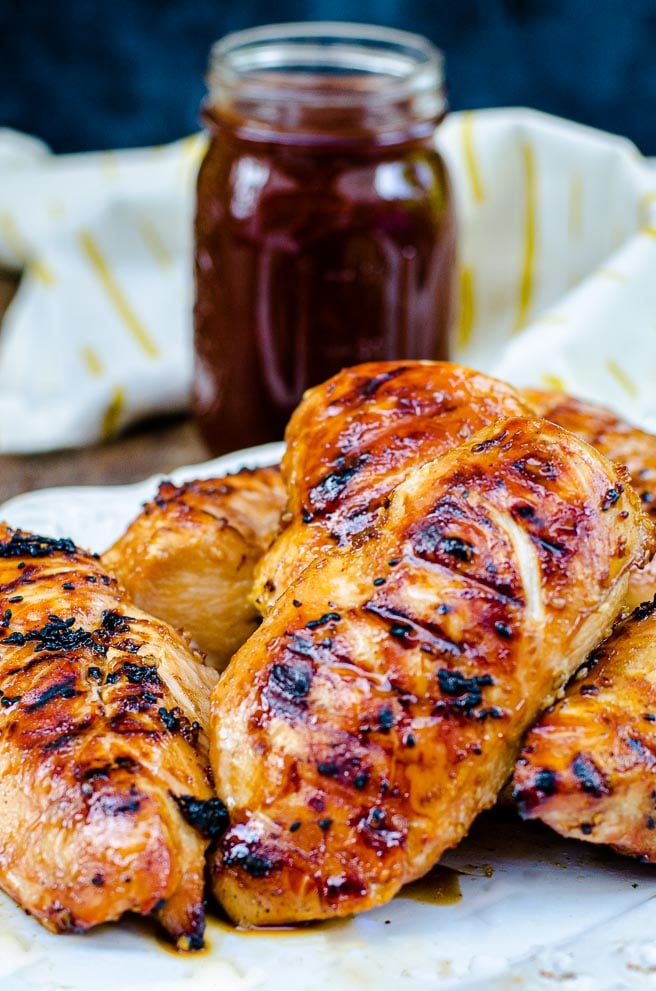 a plate of bbq chicken in front of a jar of sauce