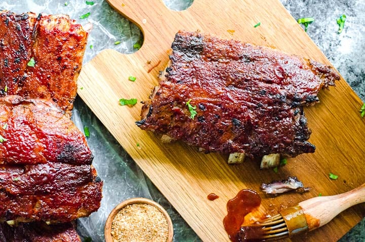 A cutting board with cooked meat and barbecue sauce on it.