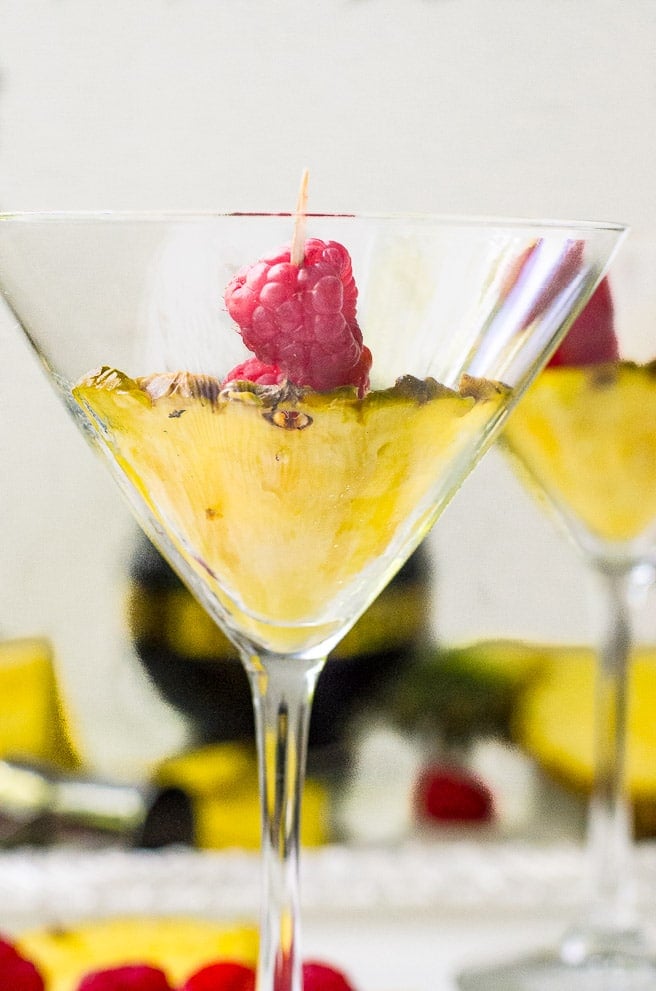 Fresh pineapple and raspberry garnish inside of a cocktail glass.