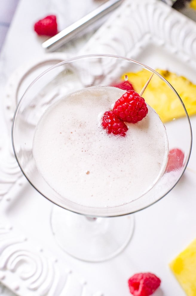 Overhead view of the inside of a cocktail glass garnished with raspberries. It shows the foam from shaking instead of stirring the drink.