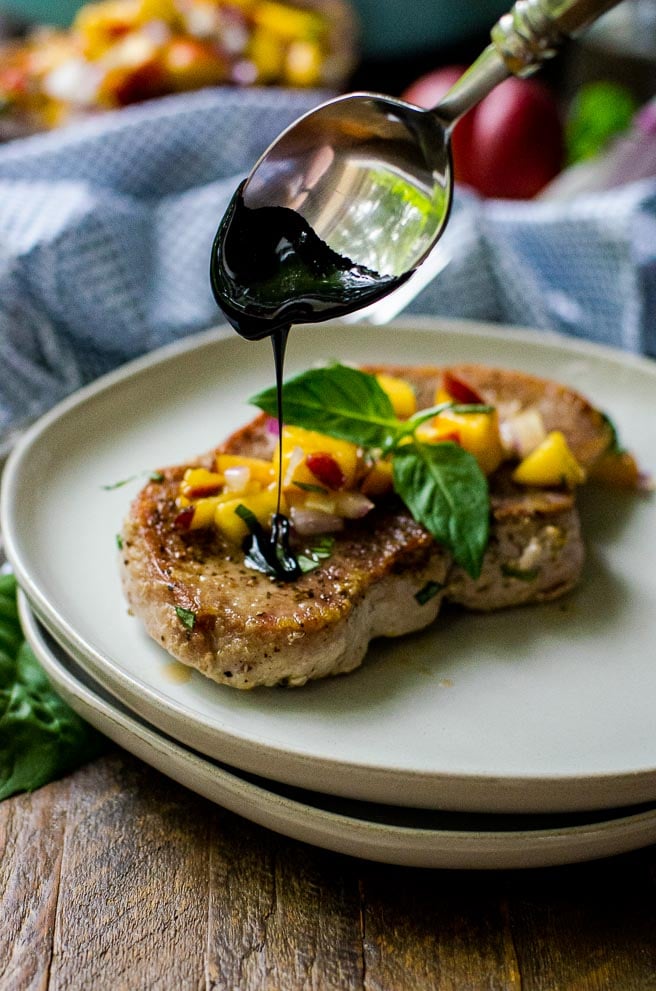 A spoon drizzling balsamic glaze onto a pork chop.