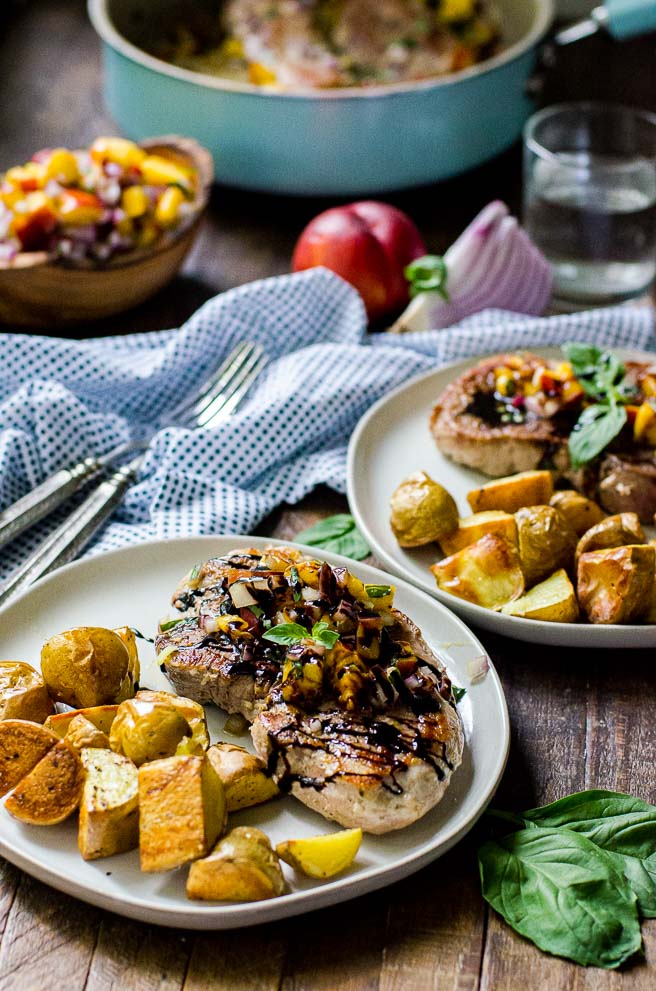 two plates of pork chops and roasted potatoes next to a polka dotted napkin.