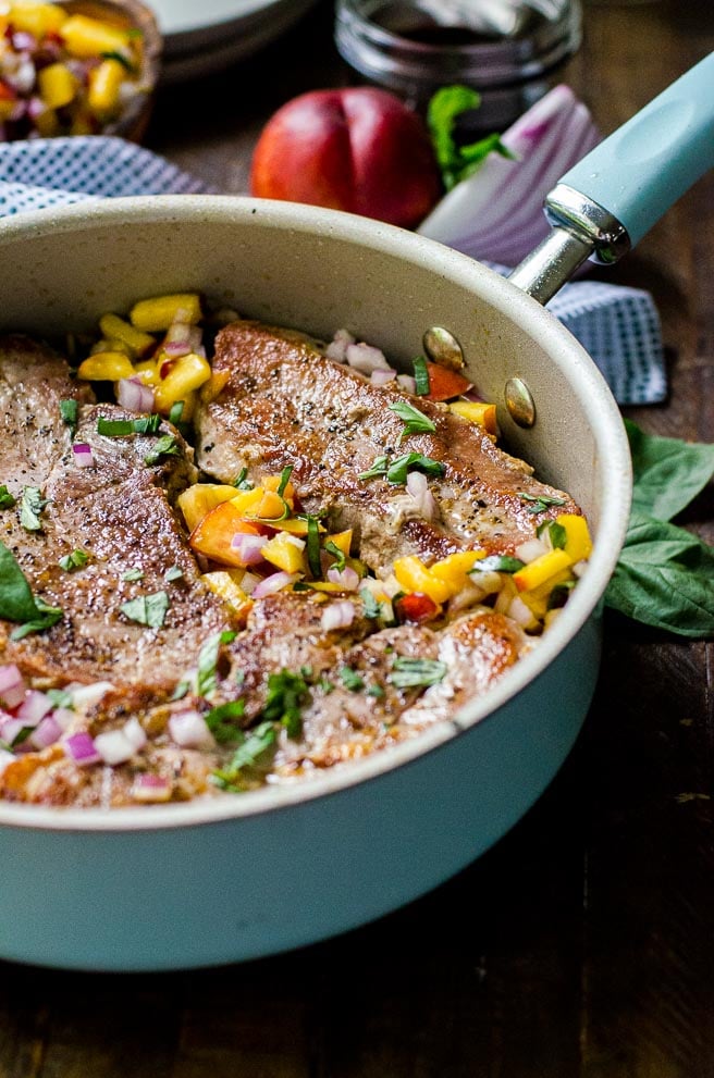 A blue skillet filled with pan seared pork chops and with nectarines