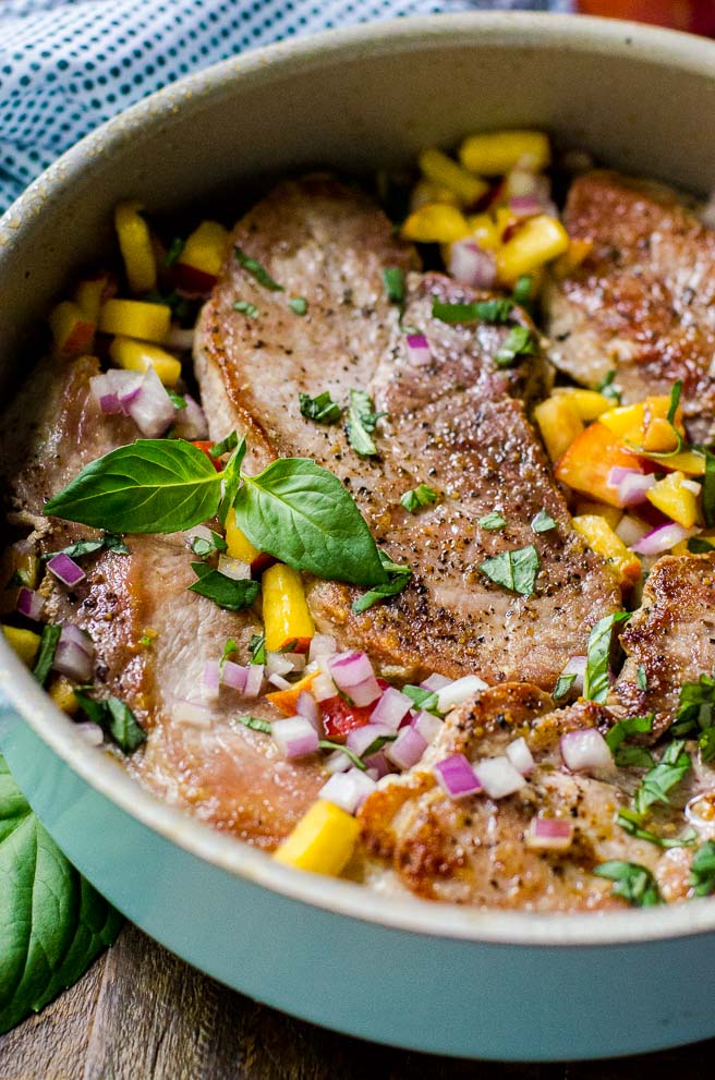 Pan seared pork chops in a pan with a basil garnish