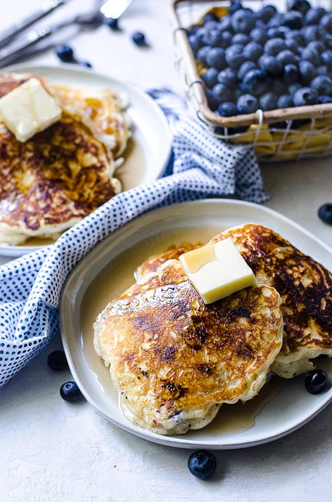 Two plates of blueberry pancakes topped with butter and syrup.