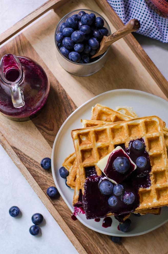 overhead view of a breakfast tray of waffles, blueberries, and syrup.