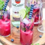 Two glasses of blueberry mojito in front of a bottle of bacardi rum.