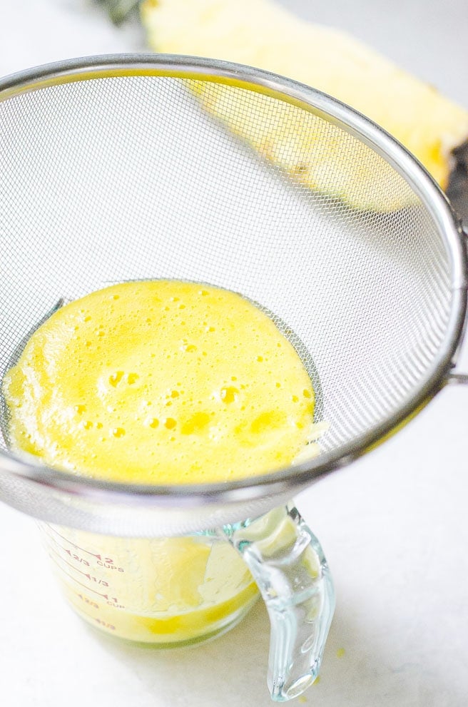 A sieve being used to remove pulp from the pineapple juice.