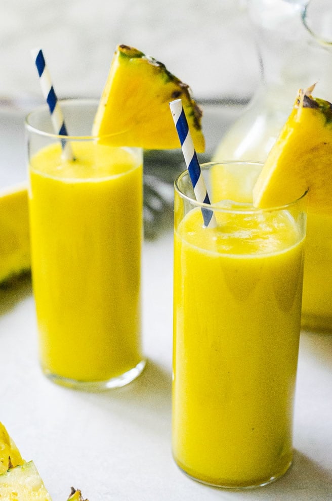 Two glasses of pineapple juice in front of a pitcher.