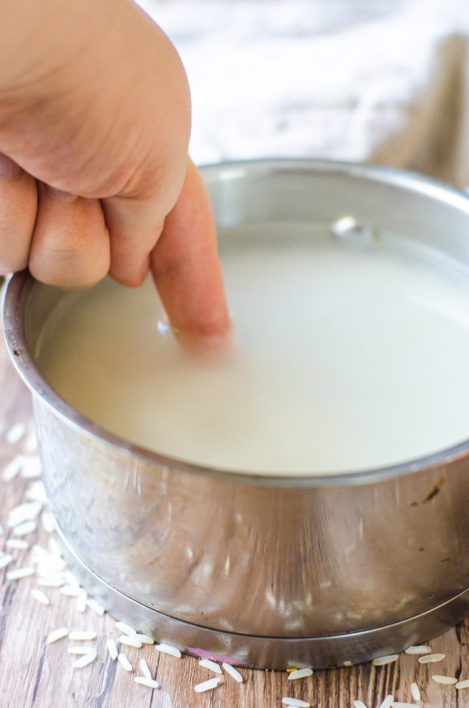 A finger being dipped into rice water for making perfect white rice.