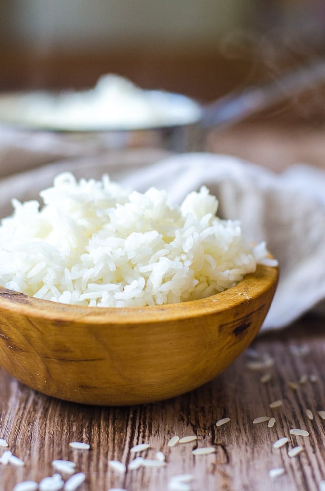 a wooden bowl overflowing with cooked white rice.