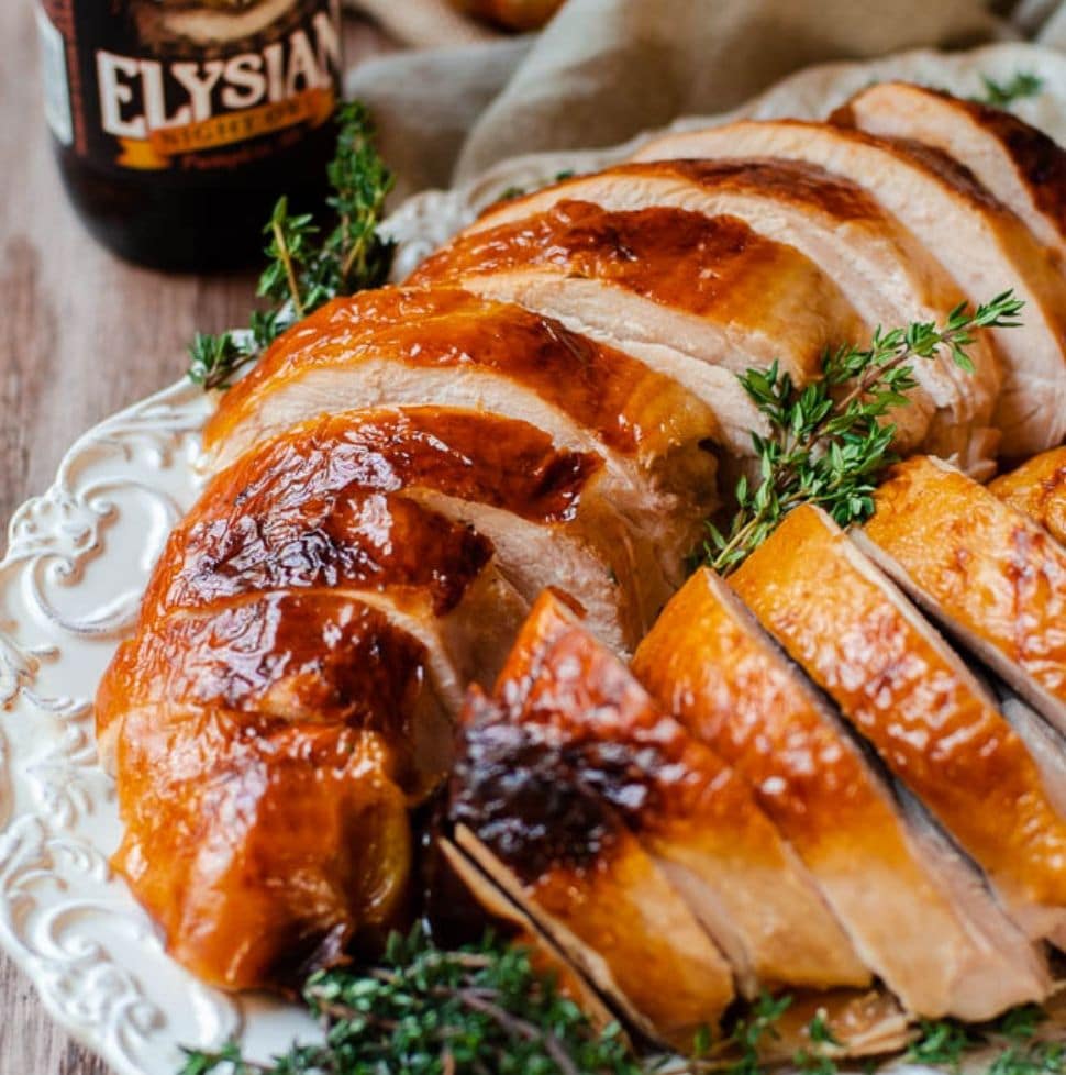 Carved Thanksgiving turkey on a white tray with a bottle of pumpkin beer behind it.