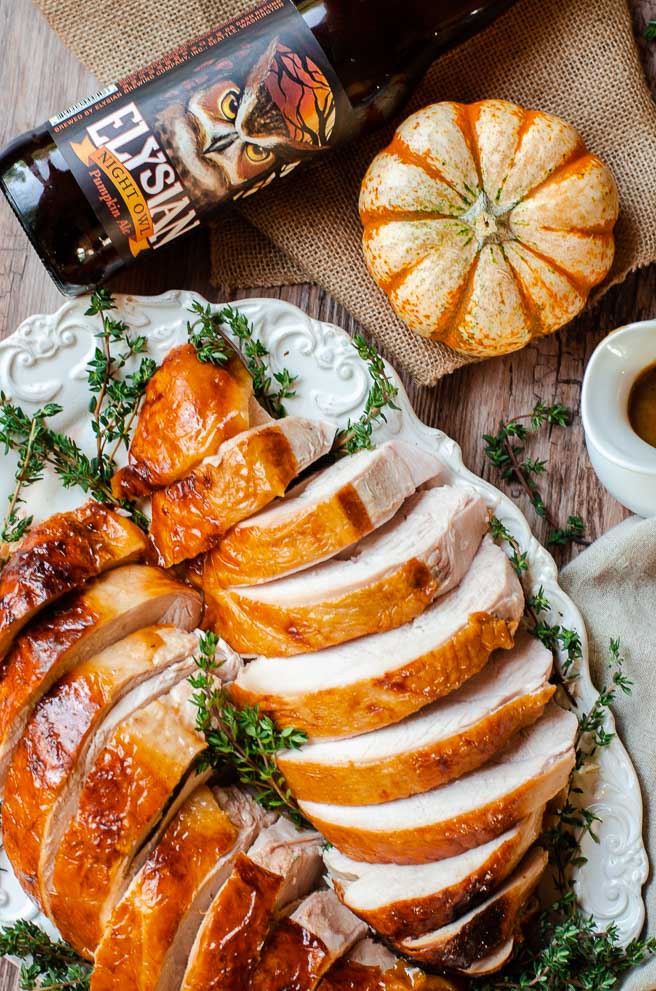 Overhead view of a bottle of pumpkin beer next to a plate of sliced Thanksgiving turkey.