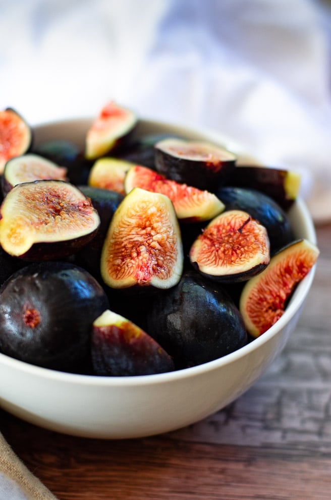 A white bowl filled with cut fresh mission figs being prepared for salad.