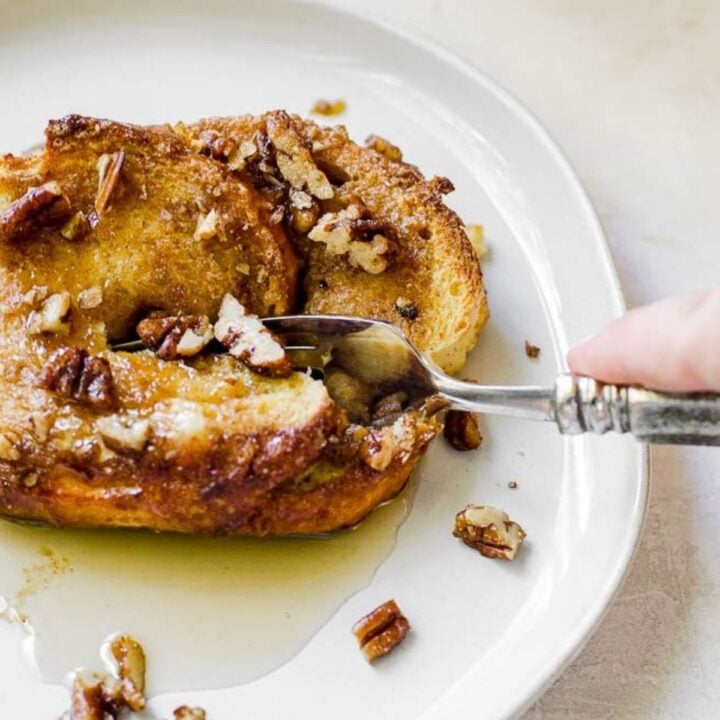 A spoon cutting into a piece of French toast adorned with pecans