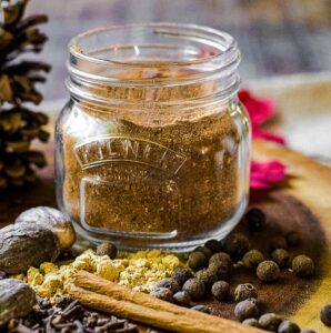 A small spice jar filled with homemade pumpkin spice blend next to the ingredients for making it.