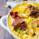 Half of a white farmhouse bowl filled to the top with pumpkin soup and toppings.