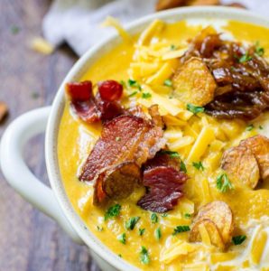 Half of a white farmhouse bowl filled to the top with pumpkin soup and toppings.