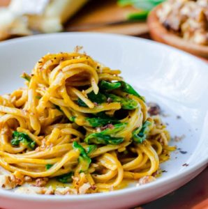 Creamy pumpkin pasta and spinach piled and swirled up high on a white plate.