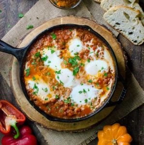 A cast iron skillet of pumpkin shakshuka surrounded by the ingredients used to make it.