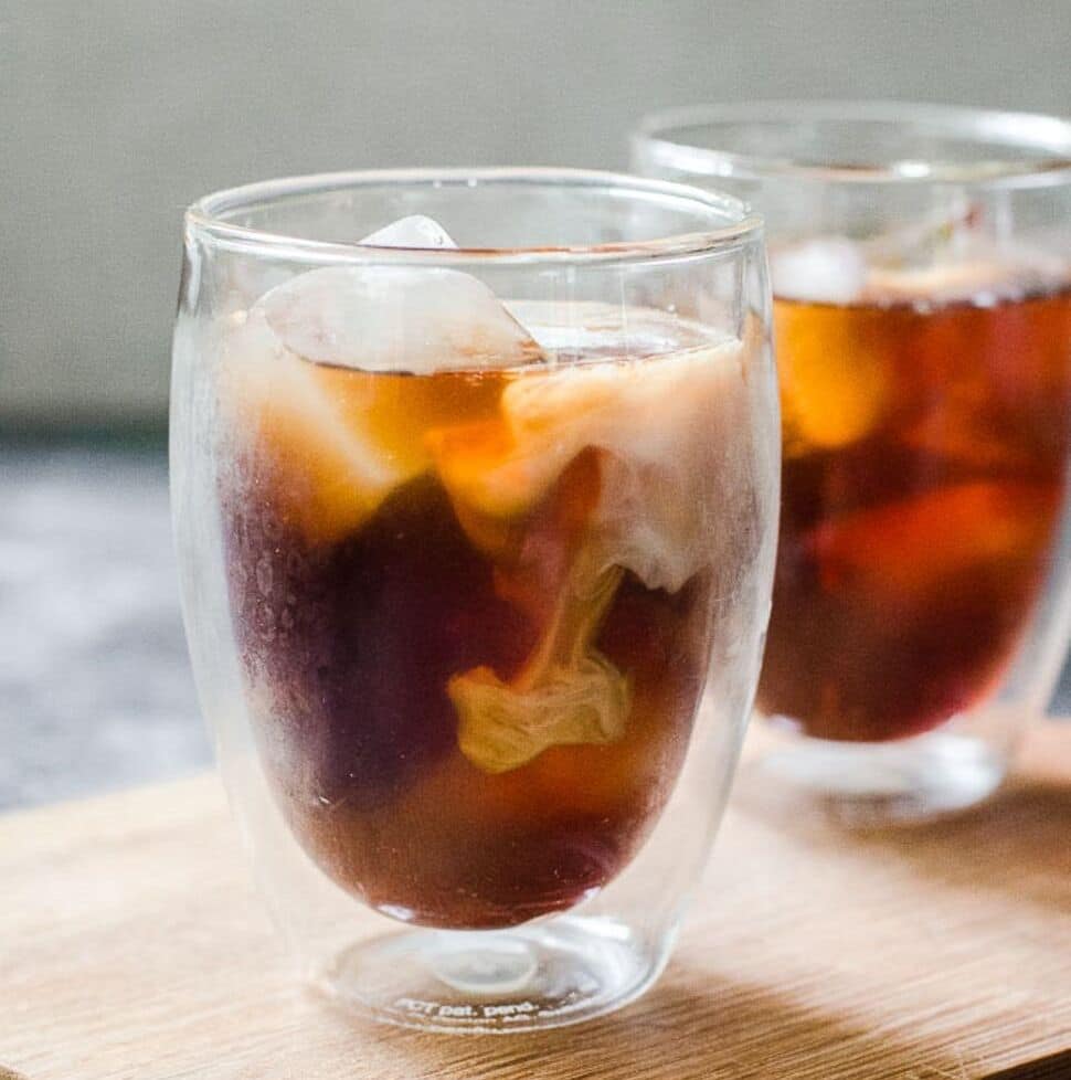 Cream swirling in a clear cup of iced cold brew coffee.