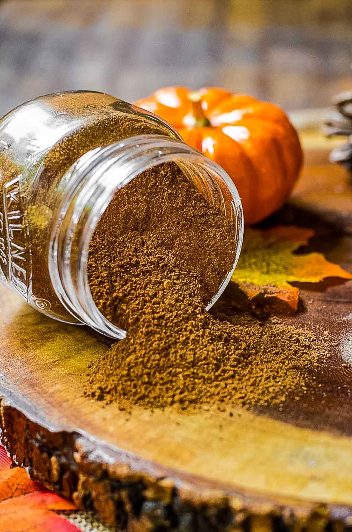 Homemade pumpkin pie spice spilling out of a jar onto a piece of wood.