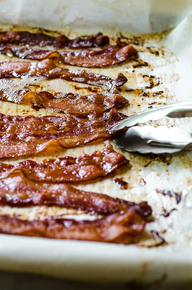 Tongs picking up bacon out of bacon fat.