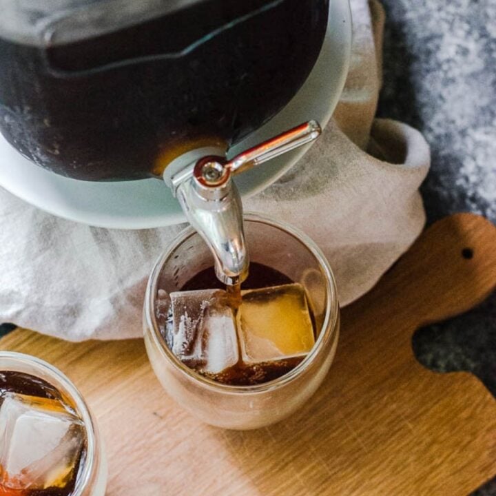 A glass jug actively pouring a brown, iced cold brew
