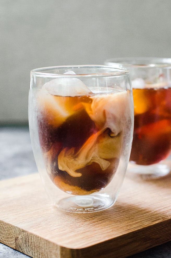Cream swirling through a clear cup of cold brew coffee.