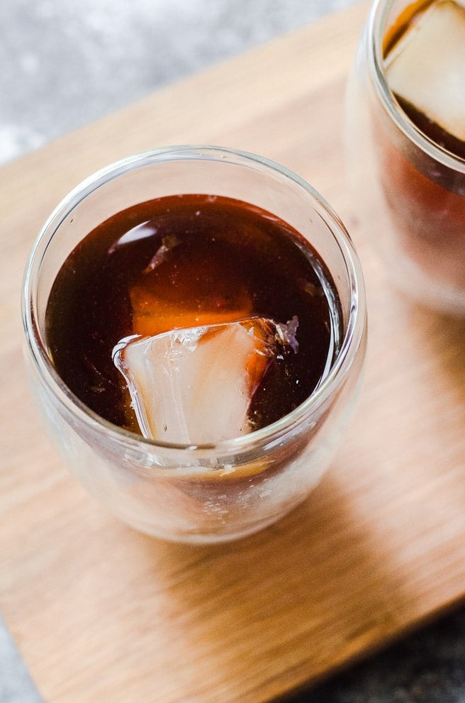 A square ice cube sticking out of clear glass of coffee.