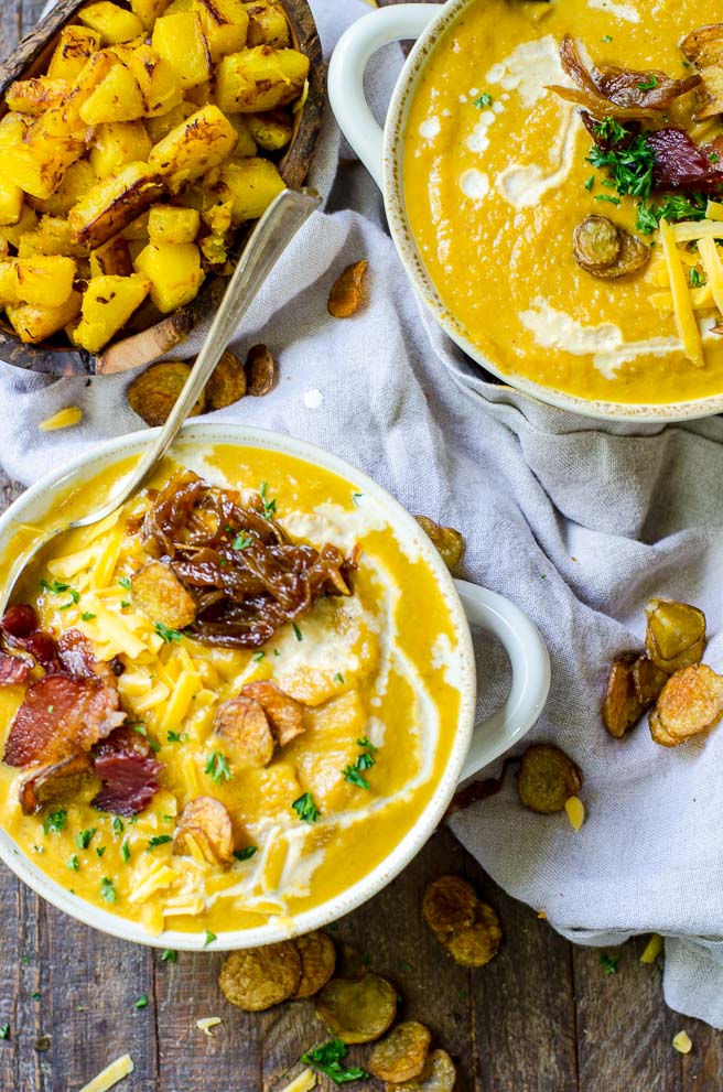 Two bowls of loaded pumpkin soup surrounded by numerous toppings.  