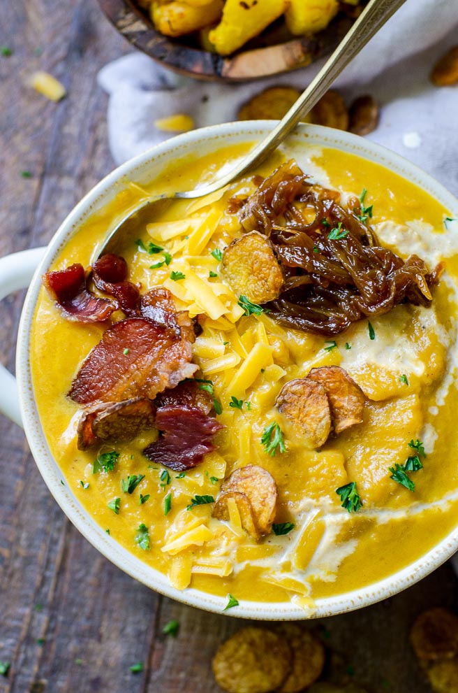 Overhead view of a bowl of pumpkin soup that is drizzled with cream and topped with bacon, caramelized onions, and 